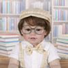 Close up of Handsome School Boy Charlie Brooks realistic reborn toddler with glasses and plaid cap in a library setting