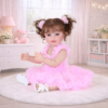 Happy Dance 22-inch reborn toddler girl doll with rooted brown pigtails and a plush white bunny sitting in a pink nursery wearing a ruffled pink dress