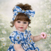 Sweet Dreams Daisy reborn doll close-up in garden setting with brown curls blue floral dress and soft expression