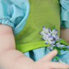 Exquisite detail of Meadow Grace’s green and blue fairy-inspired dress with artisan floral accents.