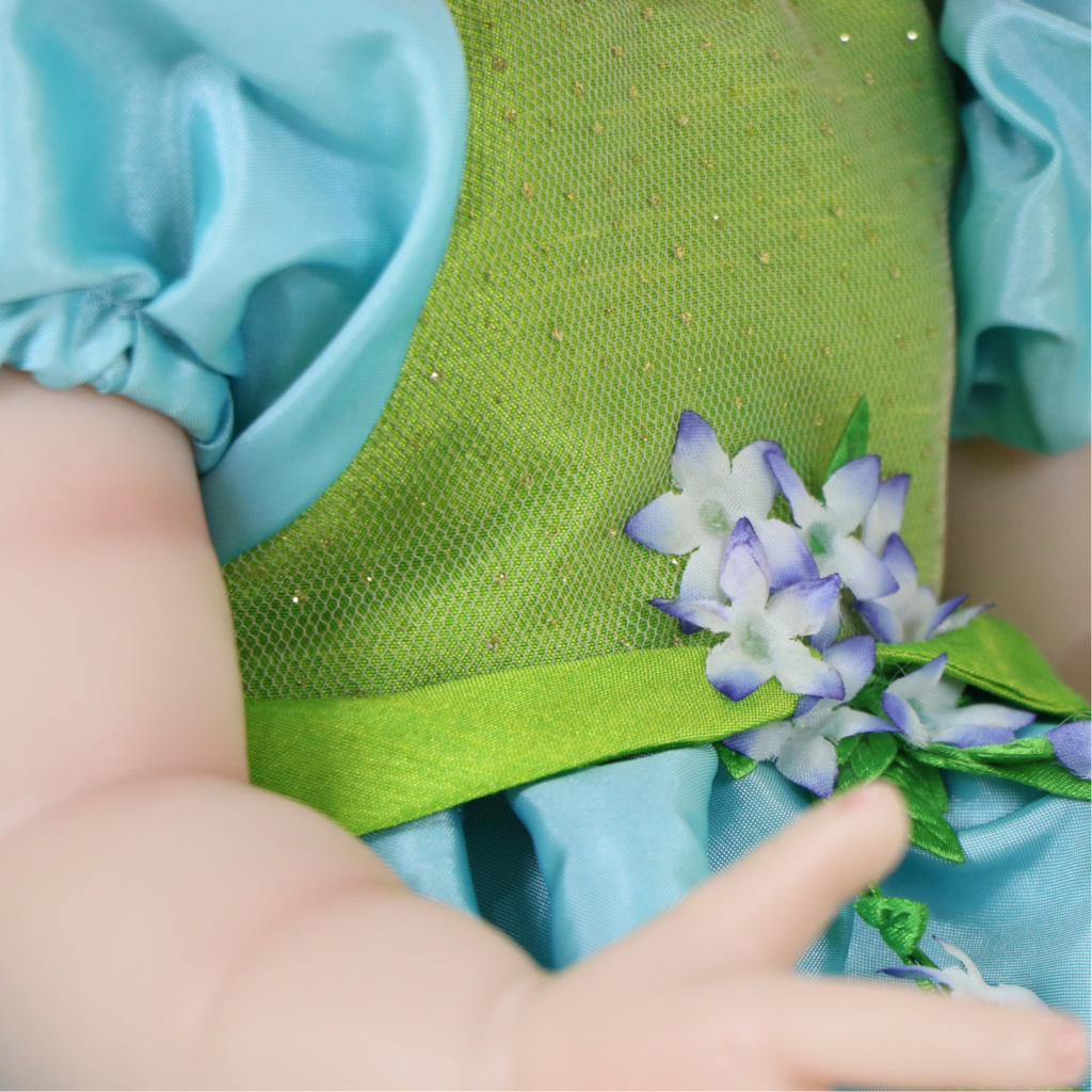 Exquisite detail of Meadow Grace’s green and blue fairy-inspired dress with artisan floral accents.