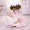 Clara Bloom reborn doll sitting in nursery with pink pacifier baby bottle and soft background decor