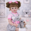 Reborn baby doll seated in nursery setting with koala plush and bottle, lifelike toddler doll for play and display
