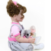 Side view of reborn baby doll holding koala plush toy and baby bottle, full vinyl toddler doll