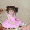Madison reborn toddler doll in pink ruffle dress sitting on chair with curly brown pigtails