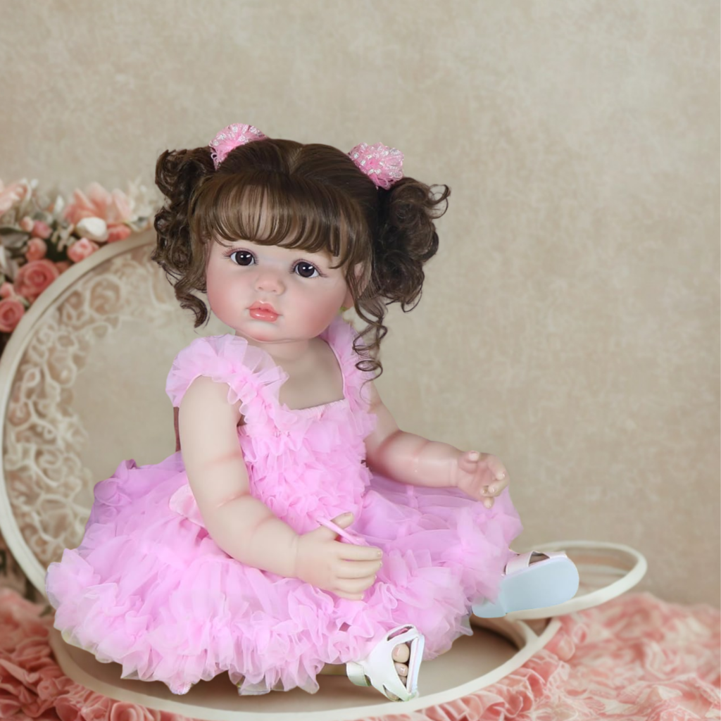 Madison reborn toddler doll in pink ruffle dress sitting on chair with curly brown pigtails