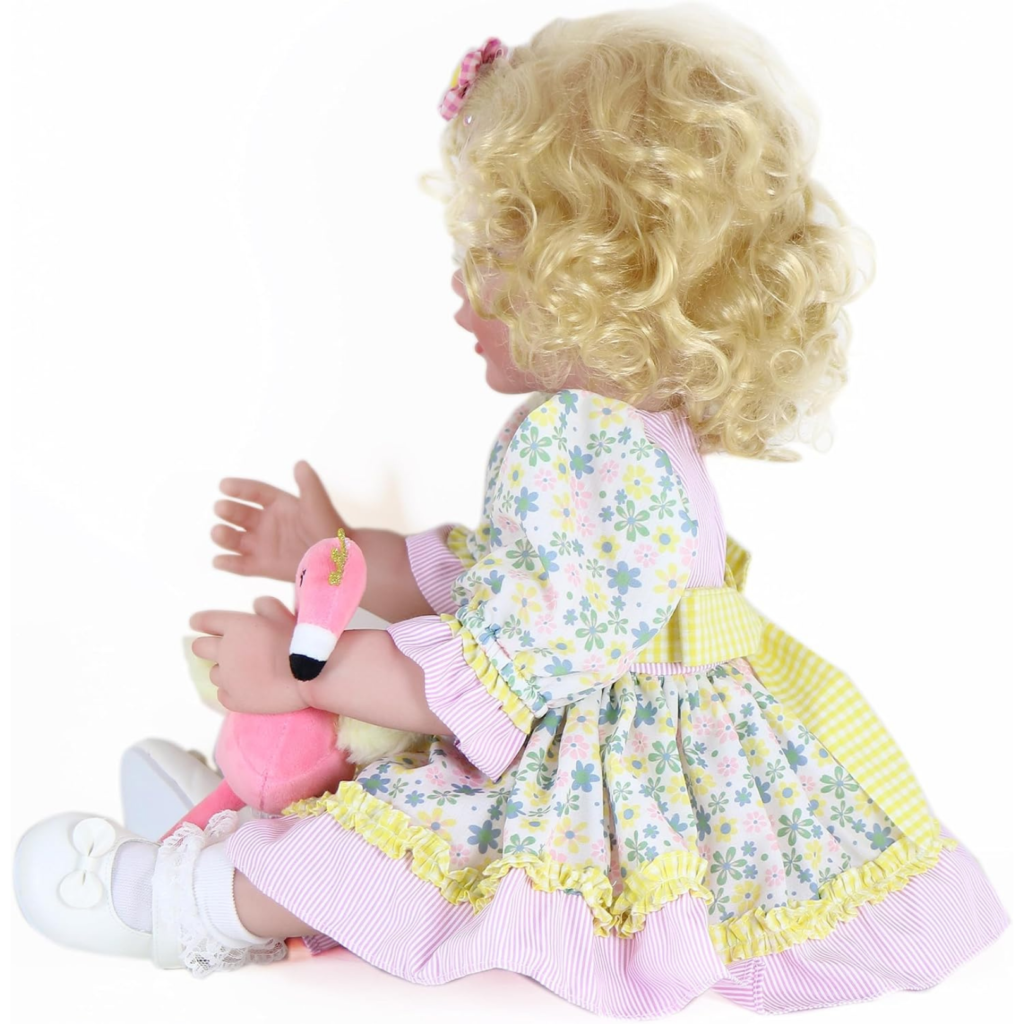side view of Sunny Flamingo Girl reborn toddler doll with blonde curls holding pink flamingo plush wearing floral dress