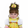 Close-up Bella Sunshine reborn baby doll with brown hair curls yellow dress and lifelike facial features