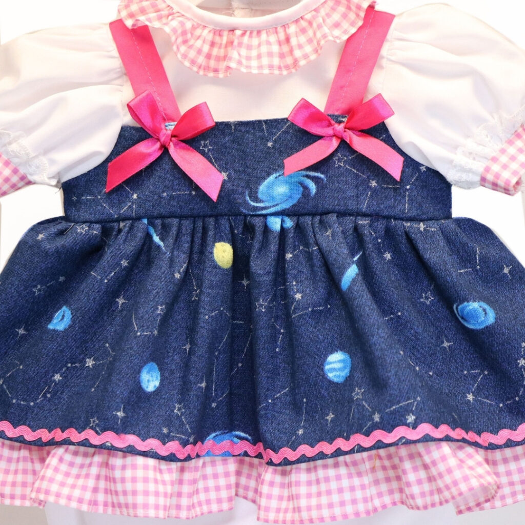 Close up galaxy print doll dress with stars planets pink trim and layered gingham ruffle