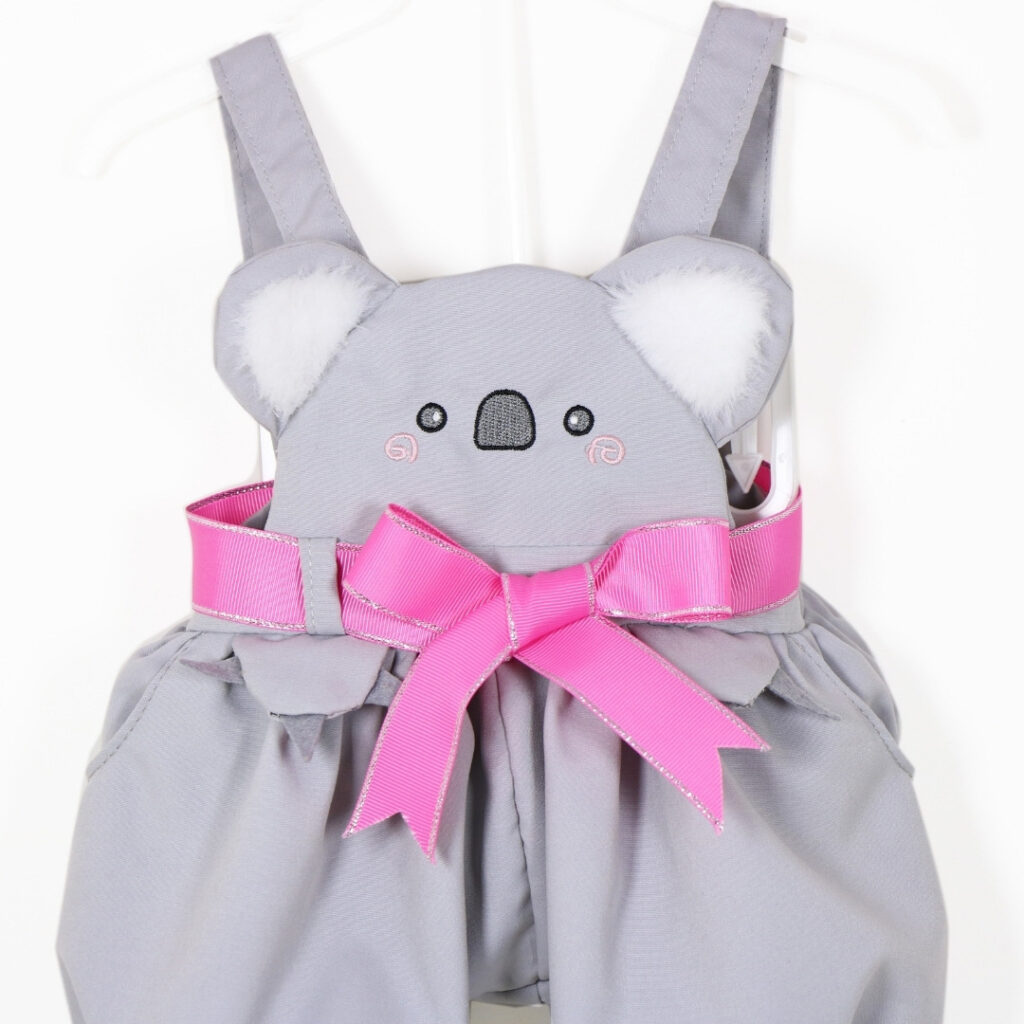 Close up of koala face design on doll outfit with plush ears and pink bow detail