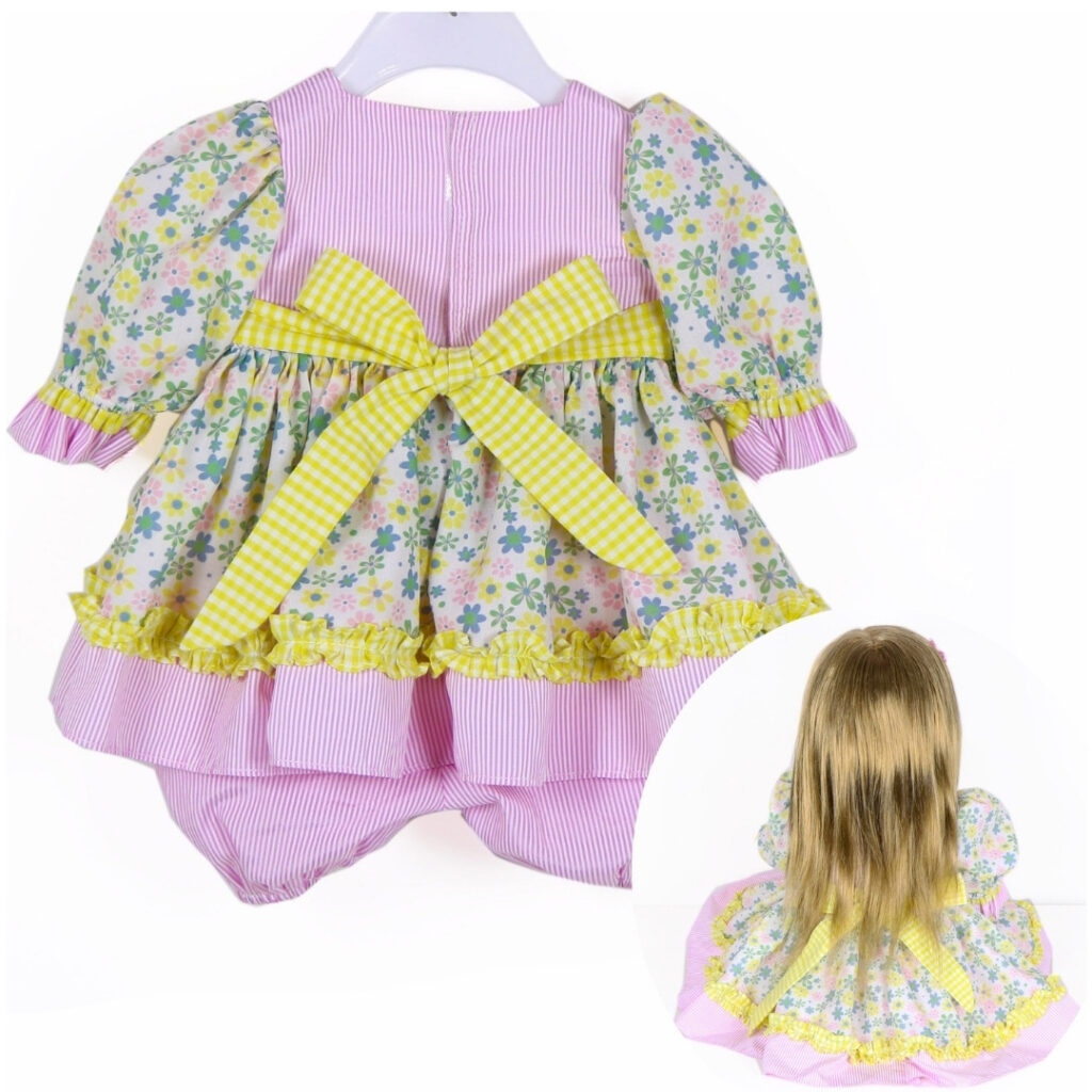 22 inch doll wearing pastel floral ruffle dress outfit with bloomers and matching flower hair accessory