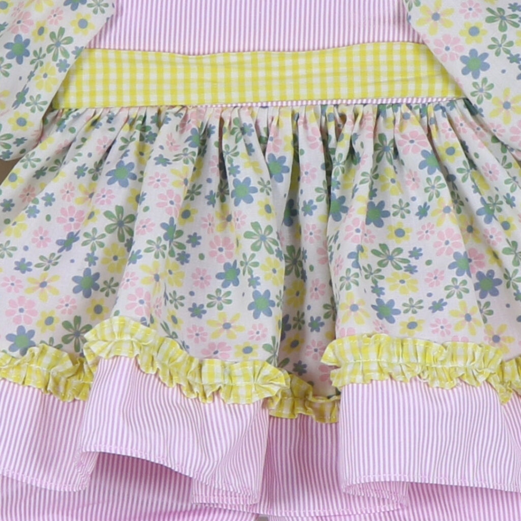 Close up of pastel floral print doll dress fabric with yellow gingham ruffle trim